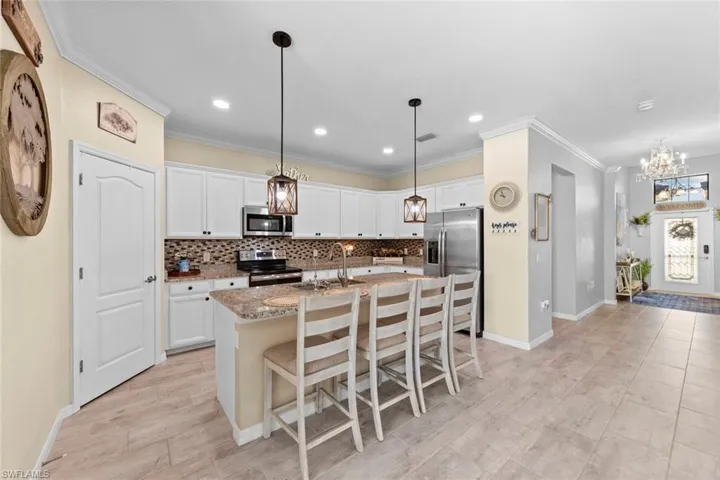 Kitchen with a kitchen island with sink, sink, crown molding, white cabinetry, and appliances with stainless steel finishes