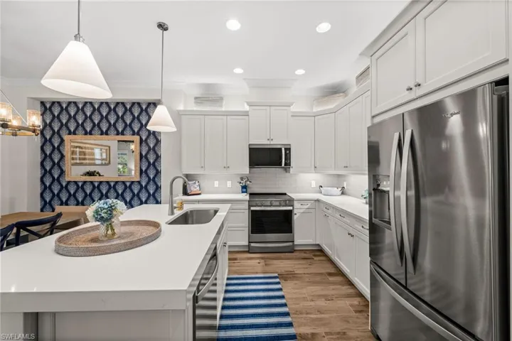 Kitchen with stainless steel appliances, ornamental molding, white cabinetry, a center island with sink, and decorative light fixtures