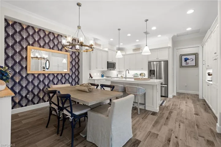 Dining area featuring light wood-type flooring, wallpapered walls, hanging lights, and ornamental molding