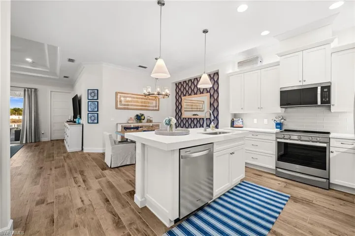 Kitchen featuring stainless steel appliances, ornamental molding, white cabinetry, backsplash, and an island with sink