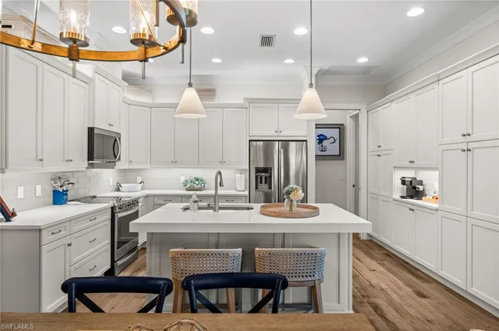 Kitchen featuring a kitchen breakfast bar, a kitchen island with sink, stainless steel appliances, white cabinets, and ornamental molding