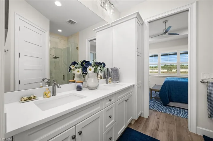 Ensuite bathroom with double vanity, light wood-type flooring, a stall shower, and recessed lighting