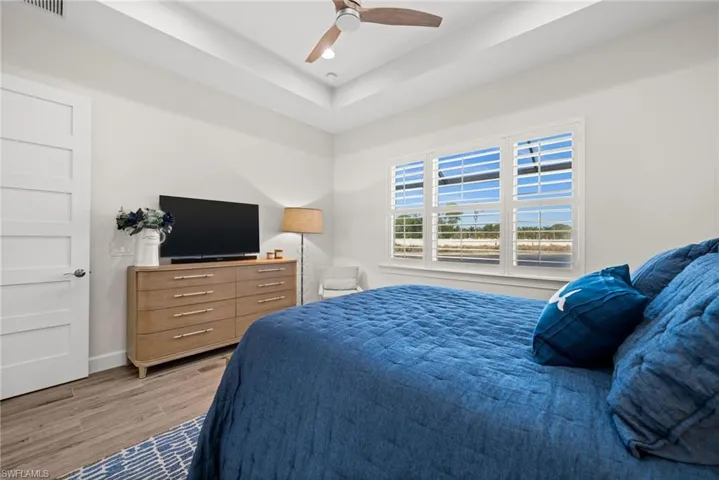 Bedroom featuring ceiling fan, light wood finished floors, and a tray ceiling