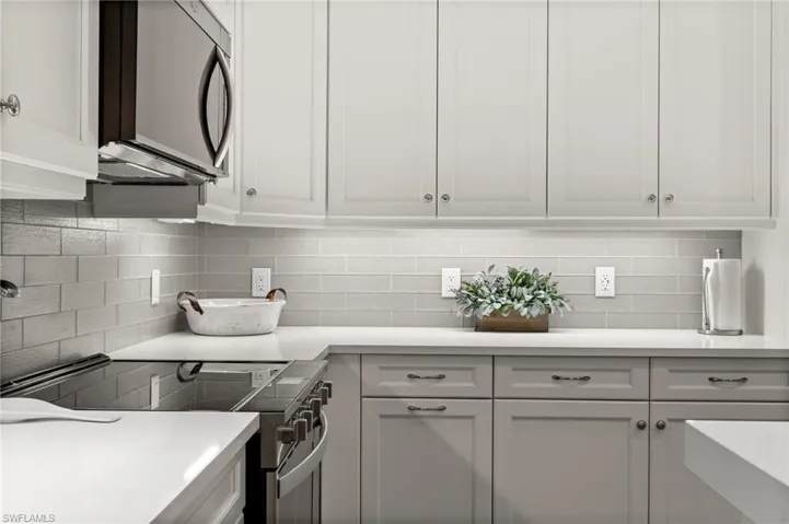 Kitchen featuring stainless steel appliances, decorative backsplash, white cabinetry, and light stone countertops