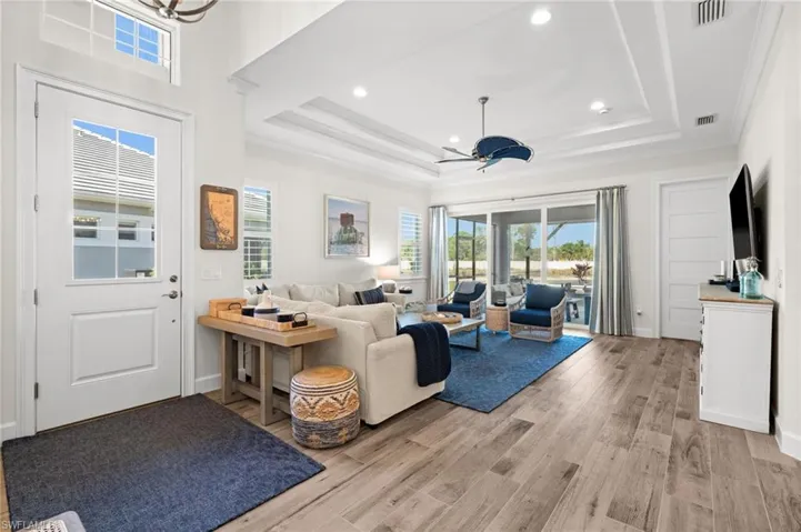 Living room with light wood-style flooring, recessed lighting, ornamental molding, a ceiling fan, and a raised ceiling