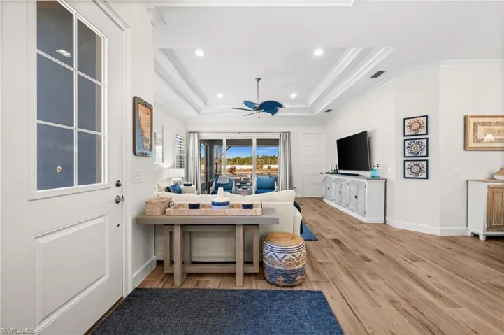 Living area with light wood-style flooring, recessed lighting, a raised ceiling, and crown molding
