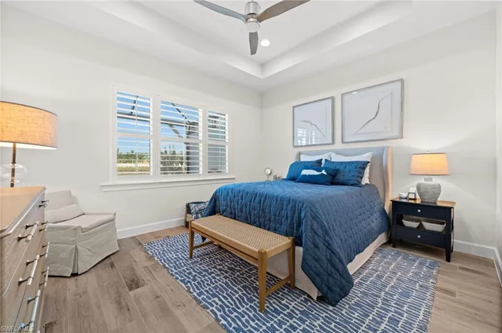 Bedroom with light wood-type flooring, a ceiling fan, a raised ceiling, and recessed lighting