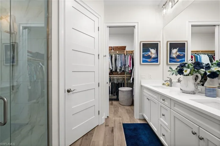 Full bathroom featuring a marble finish shower, double vanity, light wood finished floors, and a spacious closet