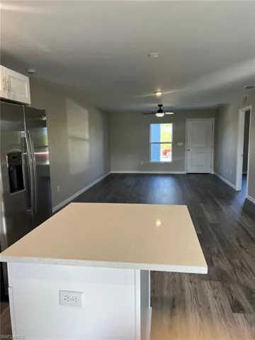 Kitchen with stainless steel fridge with ice dispenser, white cabinetry, open floor plan, dark wood finished floors, and light stone counters