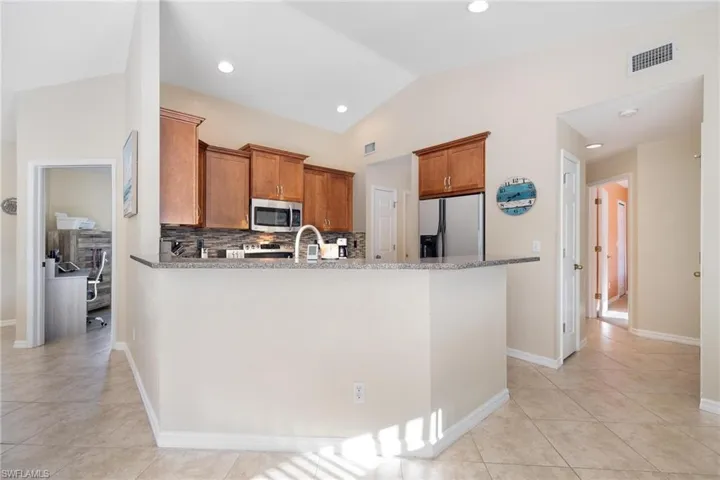 Kitchen featuring light tile patterned flooring, stainless steel appliances, decorative backsplash, light stone countertops, and lofted ceiling