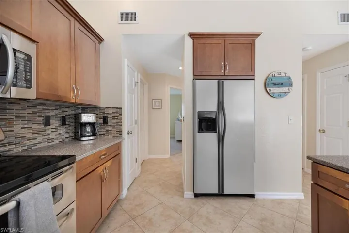 Kitchen featuring light tile patterned flooring, light stone countertops, backsplash, and stainless steel appliances