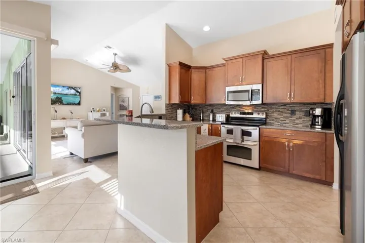 Kitchen with dark stone counters, stainless steel appliances, vaulted ceiling, tasteful backsplash, and ceiling fan