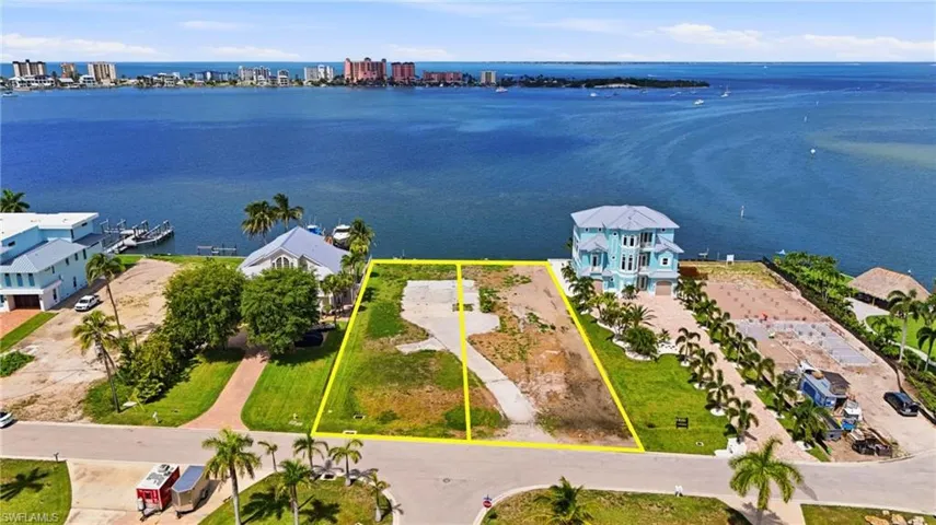 Waterfront lot with established concrete driveway, bordered by green landscaping and mature palm trees
