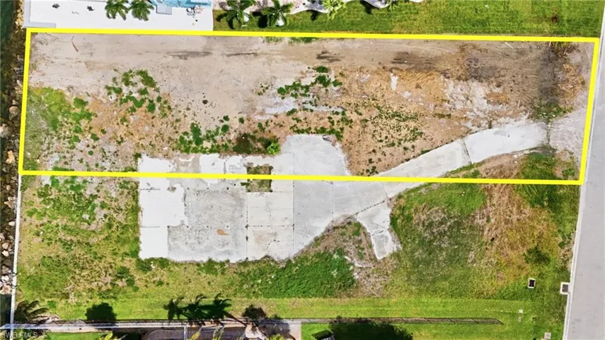 Expansive aerial view of a vacant lot with a concrete driveway and existing concrete pads