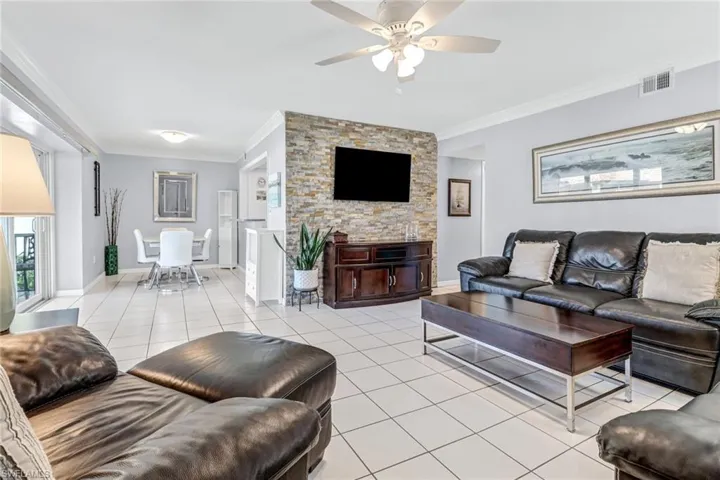 Living room featuring ornamental molding, light tile flooring, and ceiling fan