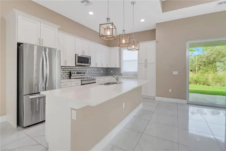 Kitchen featuring stainless steel appliances, white cabinetry, pendant light fixtures, and an large island