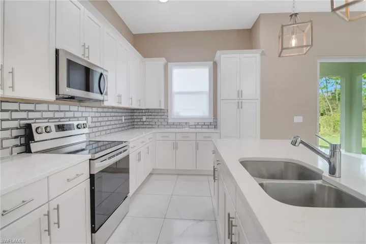Kitchen featuring stainless steel appliances, decorative backsplash, pendant light fixtures, and white cabinetry