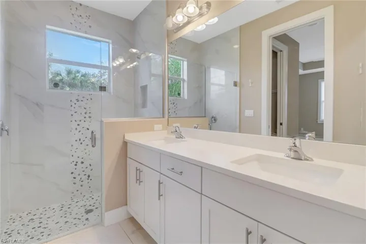 Upgraded main bathroom featuring glassed tile shower with stone accents and vanity with dual sinks