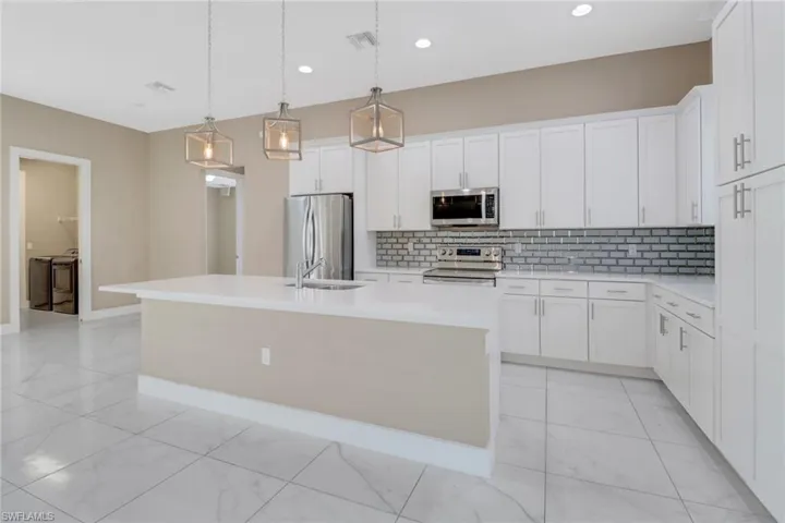 Kitchen with white cabinetry, a center island with sink, stainless steel appliances, and decorative light fixtures