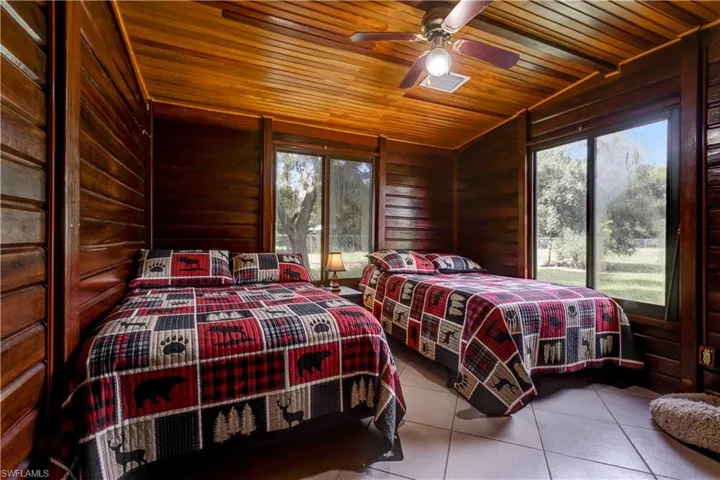 Bedroom with wood walls, tile patterned flooring, wood ceiling, and ceiling fan
