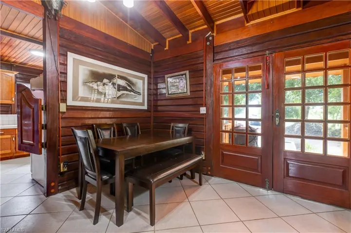 Dining room featuring wooden walls, tile patterned flooring, and a wooden ceiling with exposed beams