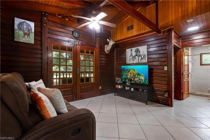 Living room featuring wood walls, ceiling fan, light tile patterned floors, and a wooden ceiling with exposed beams