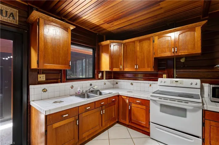 Kitchen featuring white electric range, brown cabinetry, tile countertops, light tile patterned floors, and wooden ceiling