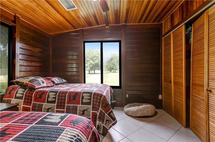 Tiled bedroom featuring wood walls, lofted ceiling, ceiling fan, wooden ceiling, and a closet