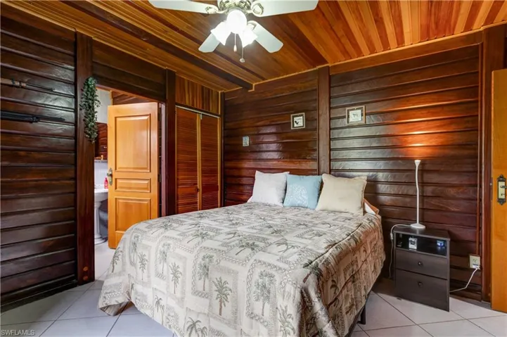 Kitchen featuring tile countertops, white appliances, light tile patterned flooring, wooden walls, and brown cabinetry