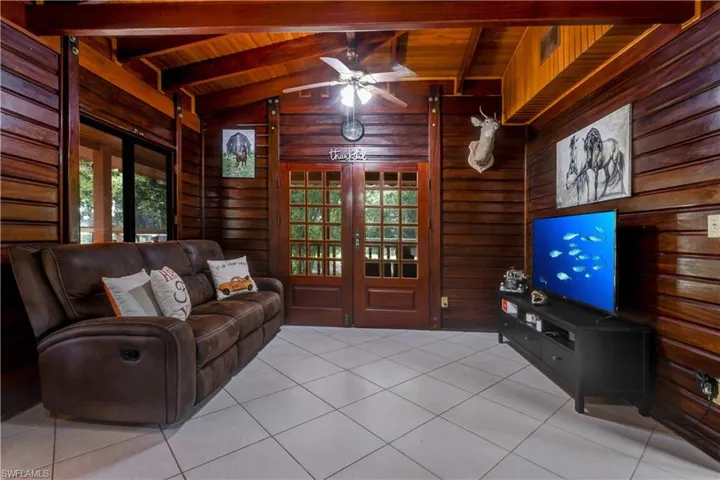 Living area with healthy amount of natural light, light tile patterned flooring, a ceiling fan, wooden ceiling, and wood walls