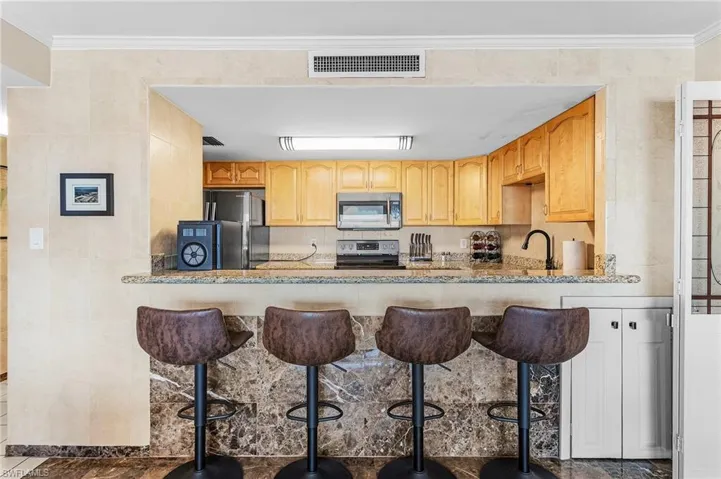 Kitchen with light stone counters, ornamental molding, visible vents, and stainless steel appliances