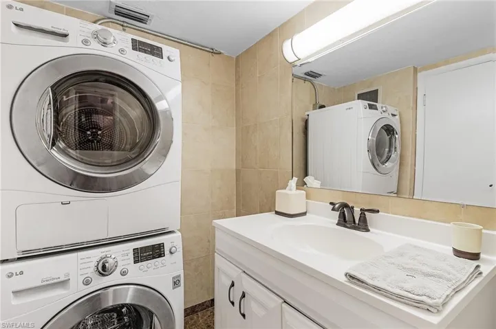 Washroom with stacked washer / dryer, laundry area, visible vents, tile walls, and a sink