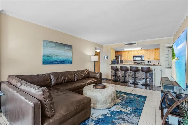 Living room with light tile patterned floors, ornamental molding, and visible vents