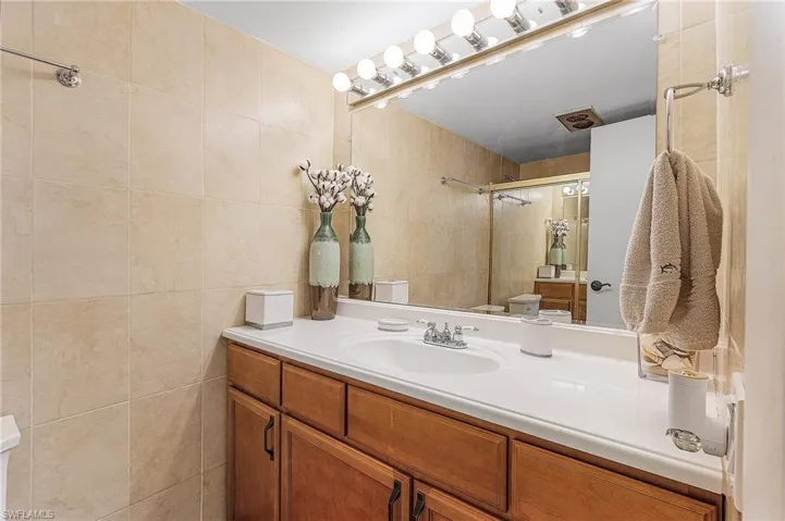 Bathroom with toilet, vanity, a shower, and tile walls