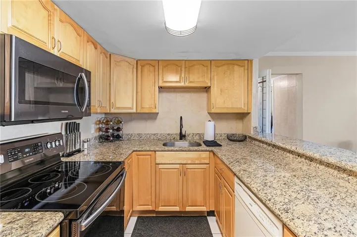 Kitchen featuring light brown cabinetry, light stone counters, a sink, white dishwasher, and electric range oven