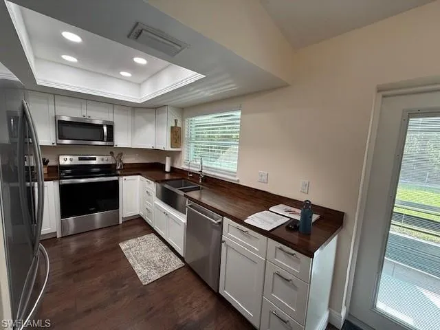 Kitchen with a raised ceiling, white cabinetry, sink, and appliances with stainless steel finishes