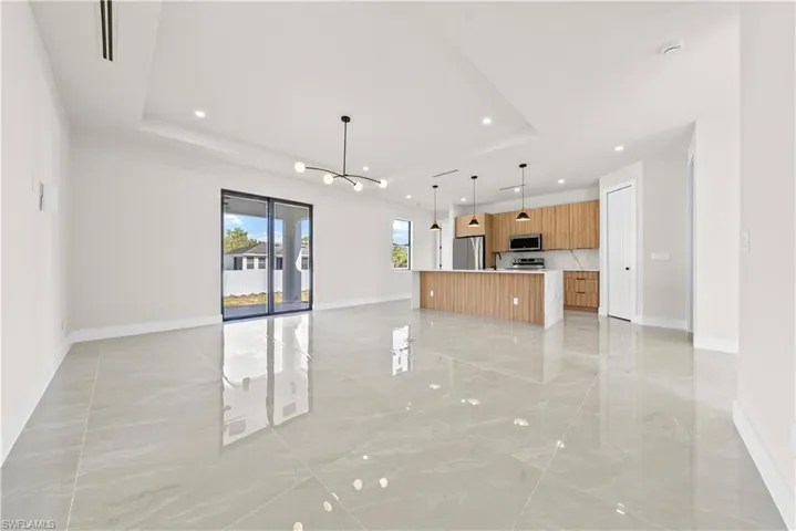 Unfurnished living room with hanging lights, light marble finish floors, and a raised ceiling