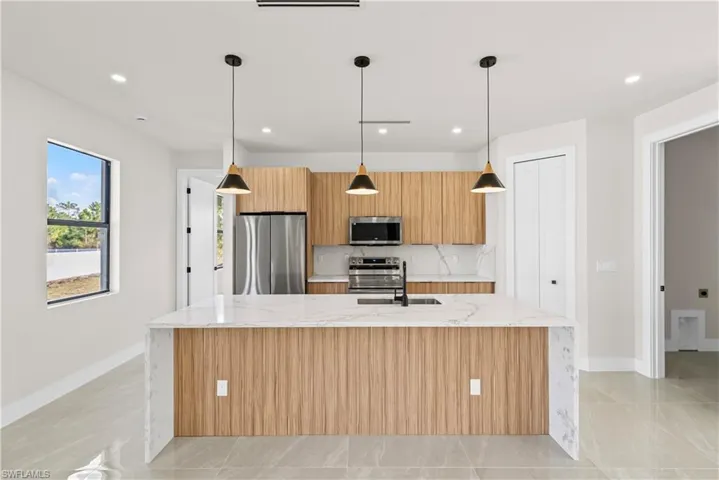 Kitchen with light stone countertops, stainless steel appliances, hanging light fixtures, a spacious island, and modern cabinets