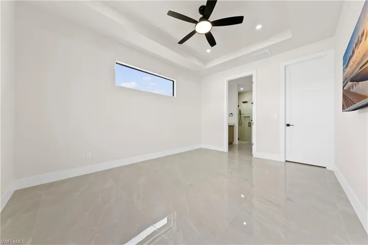 Unfurnished bedroom featuring a ceiling fan, a tray ceiling, recessed lighting, and connected bathroom