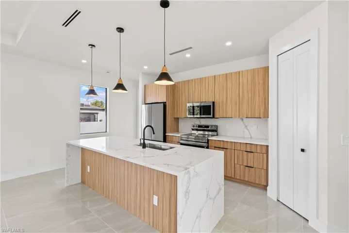 Kitchen with decorative light fixtures, stainless steel appliances, light stone counters, modern cabinets, and a center island with sink