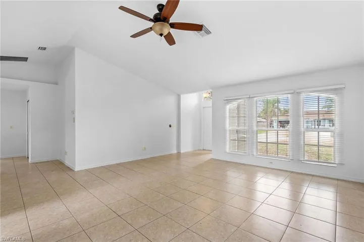 Empty room with ceiling fan, lofted ceiling, and light tile patterned flooring