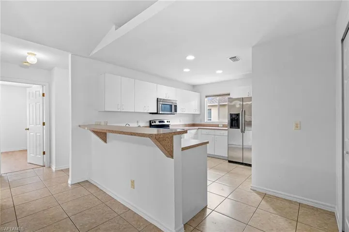 Kitchen featuring white cabinets, stainless steel appliances, a breakfast bar, a peninsula, and recessed lighting