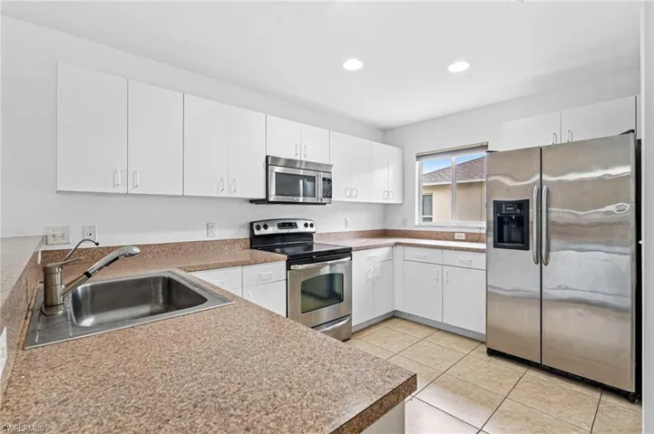 Kitchen with stainless steel appliances, white cabinets, light tile patterned floors, and recessed lighting