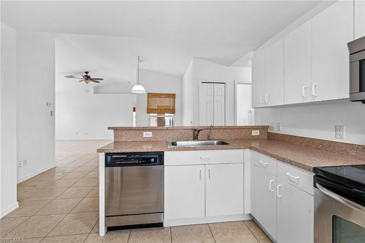 Kitchen featuring a peninsula, stainless steel appliances, white cabinets, light tile patterned floors, and ceiling fan
