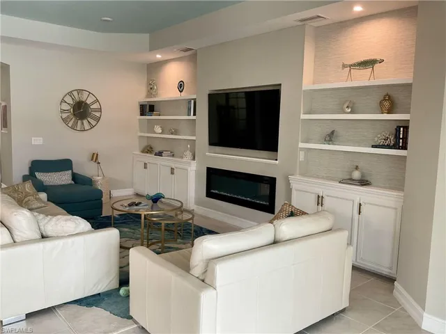 Living room featuring light tile patterned flooring, a glass covered fireplace, built in shelves, recessed lighting, and baseboards