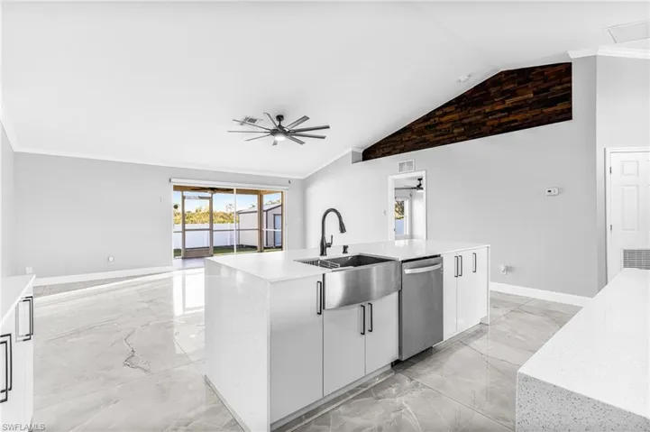 Kitchen with a center island with sink, vaulted ceiling, dishwasher, ceiling fan, and white cabinetry