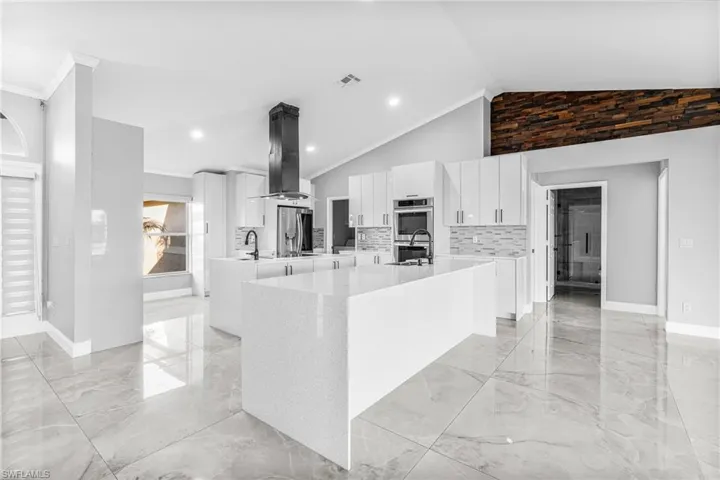 Kitchen with stainless steel appliances, white cabinets, an island with sink, crown molding, and range hood