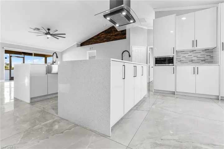 Kitchen featuring island exhaust hood, white cabinetry, stainless steel microwave, and vaulted ceiling
