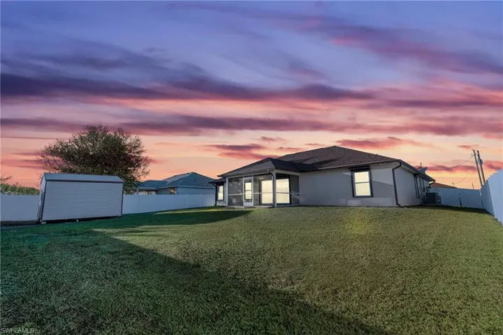 Back house at dusk with a storage unit and a lawn