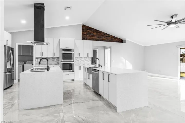 Kitchen with white cabinetry, appliances with stainless steel finishes, independent washer and dryer, an island with sink, and vaulted ceiling